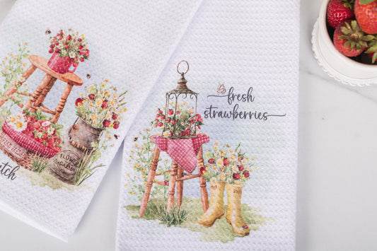 Two kitchen towels with floral and strawberry-themed designs on a white background.