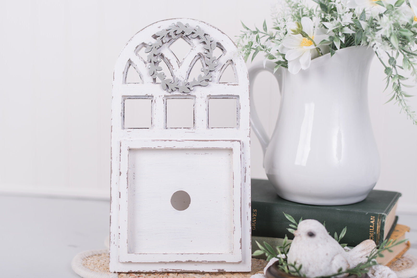 Decorative white window frame with a pitcher and flowers on a white surface