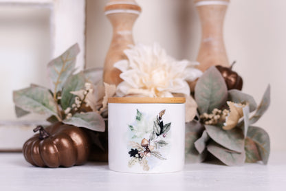 A small ceramic canister with a bamboo lid, featuring a colourful fall foliage woodland design on the front, is placed on a table with fall-themed decorations.