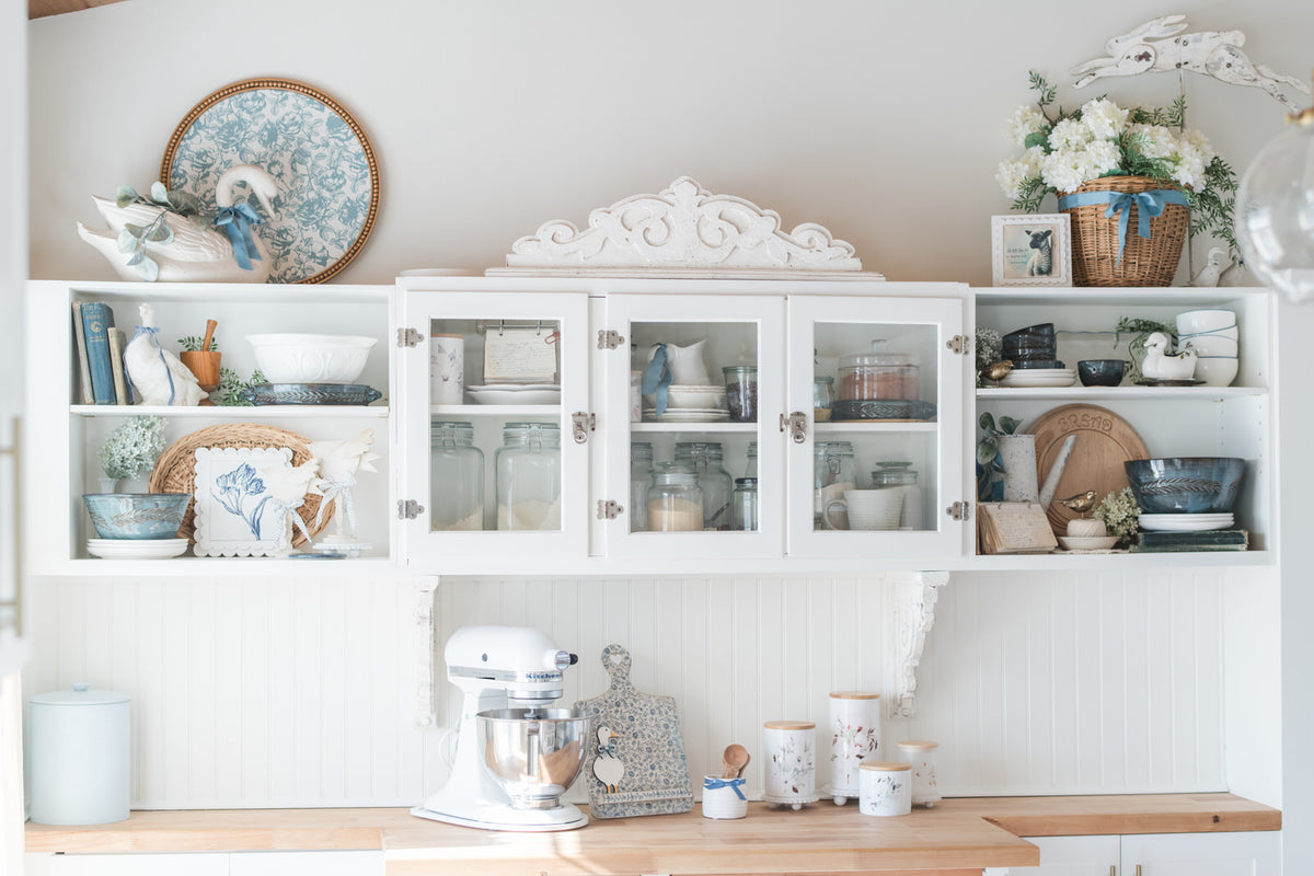 White kitchen cabinet with decorative items and a mixer on a wooden countertop.