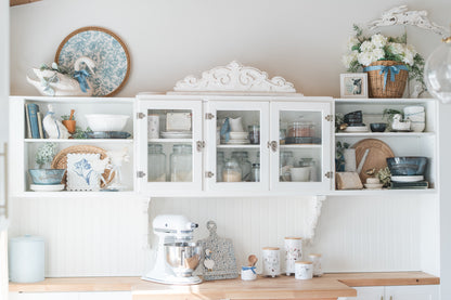 White kitchen cabinet with decorative items and a mixer on a wooden countertop.