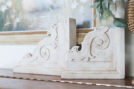 Decorative white corbels with intricate carvings on a wooden surface.