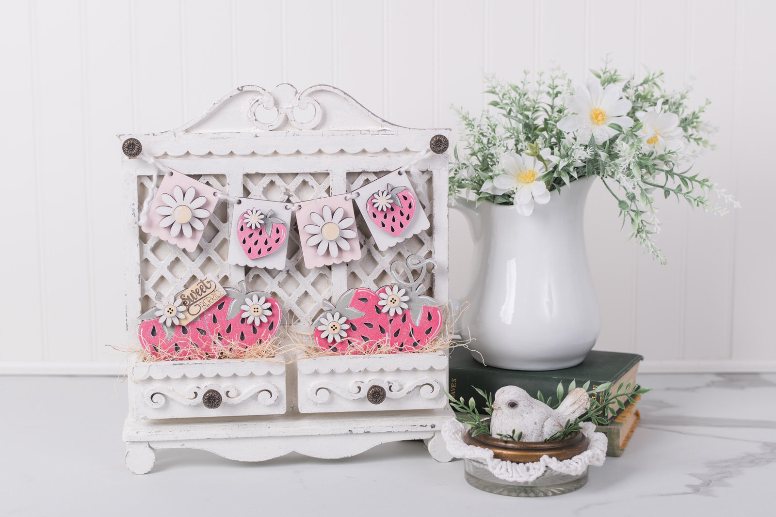 Decorative white cabinet with floral patterns, a vase with flowers, and a small figurine on a white surface.