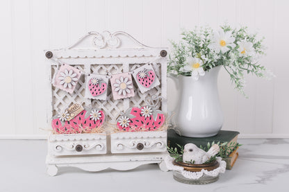 Decorative white cabinet with floral patterns, a vase with flowers, and a small figurine on a white surface.
