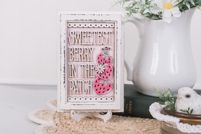 Decorative sign with 'Sweetest Berry in the Patch' text and strawberry design on a stand.