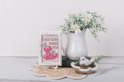 Decorative items including a framed picture, pitcher with flowers, and coasters on a white surface.