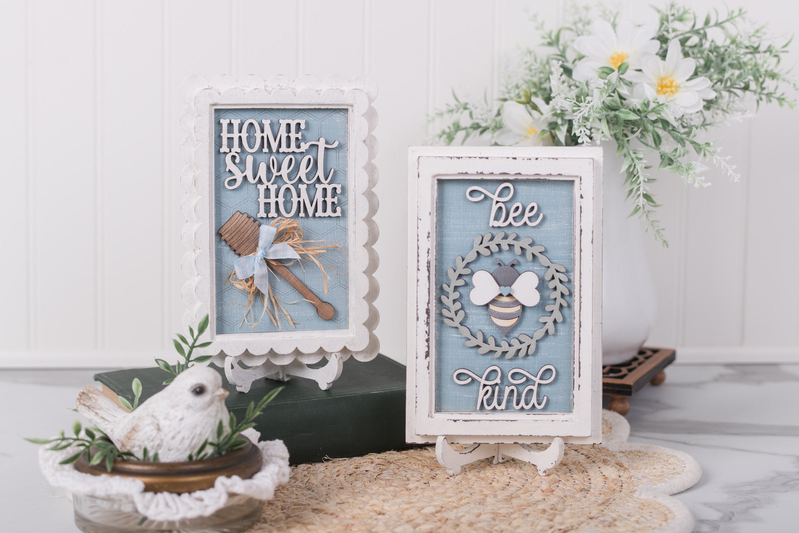 Decorative signs with 'Home Sweet Home' and 'Be kind' text, surrounded by plants and a white bird figurine.