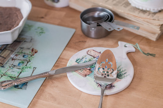 Ceramic spoon rest with soft botanical art and farmhouse vignette with knife and pie lifter resting on it