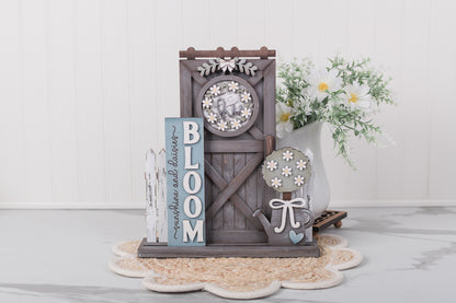 Decorative garden-themed wood porch kit with 'Bloom' sign on a white surface