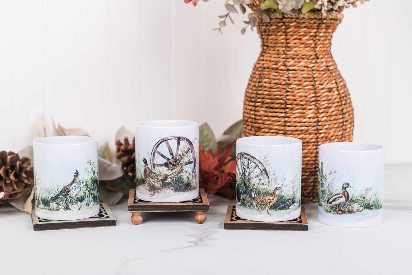 Set of four coffee mugs with game bird designs on a white surface with a woven basket in the background.