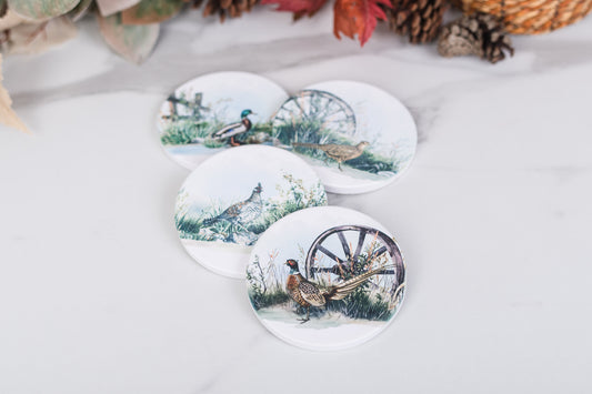 Set of four round coasters with game bird designs on a white surface.