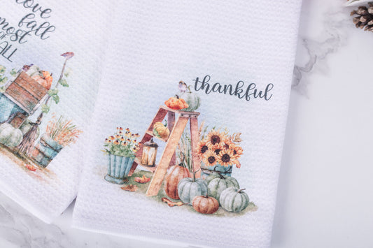 White tea towel with “Thankful” text, rustic ladder with pumpkins, lantern, and sunflowers