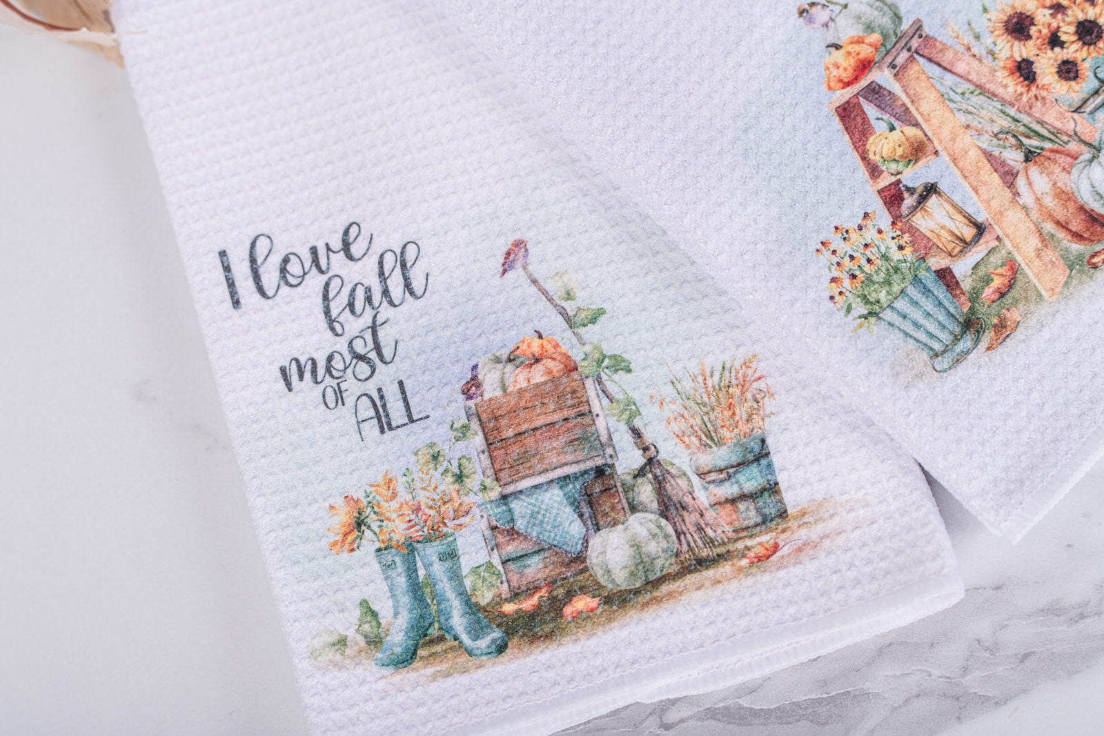 White tea towel with “I Love Fall Most of All” text, watercolor pumpkins, boots, and harvest florals