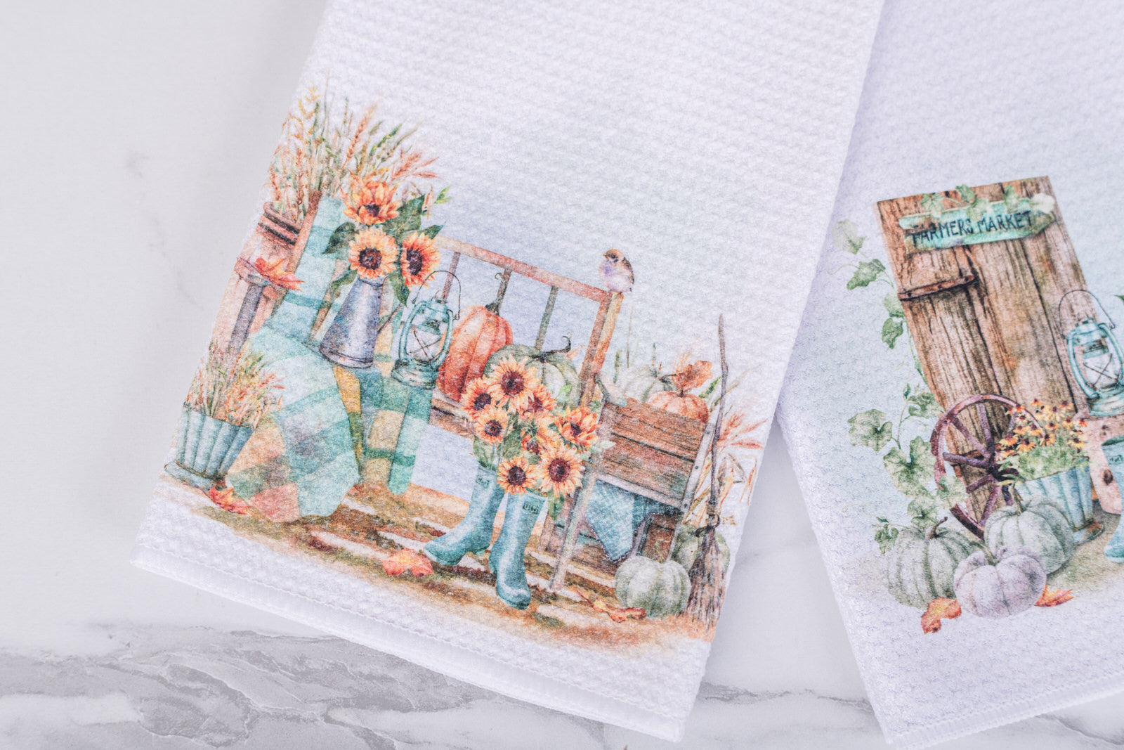 White tea towel with watercolor farmhouse porch scene, teal boots, sunflowers, and pumpkins