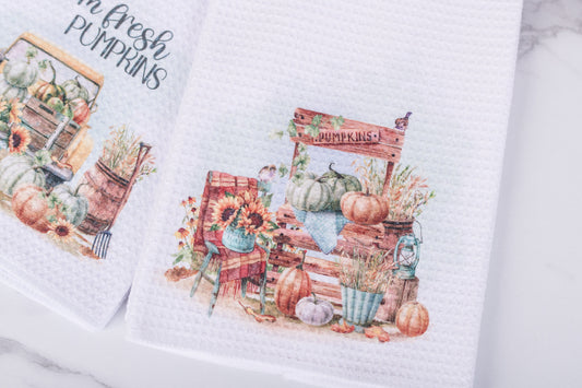 White tea towel with rustic pumpkin stand scene featuring crates, blooms, and pumpkins