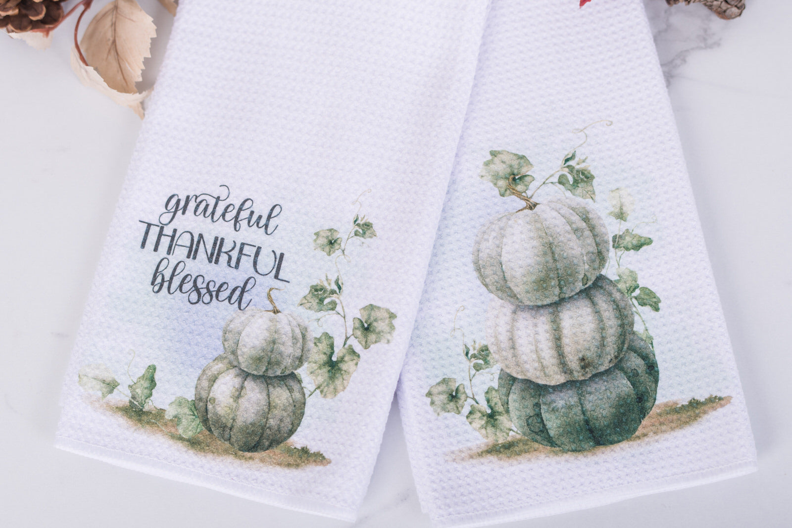 Two kitchen towels with pumpkin designs and text on a white background