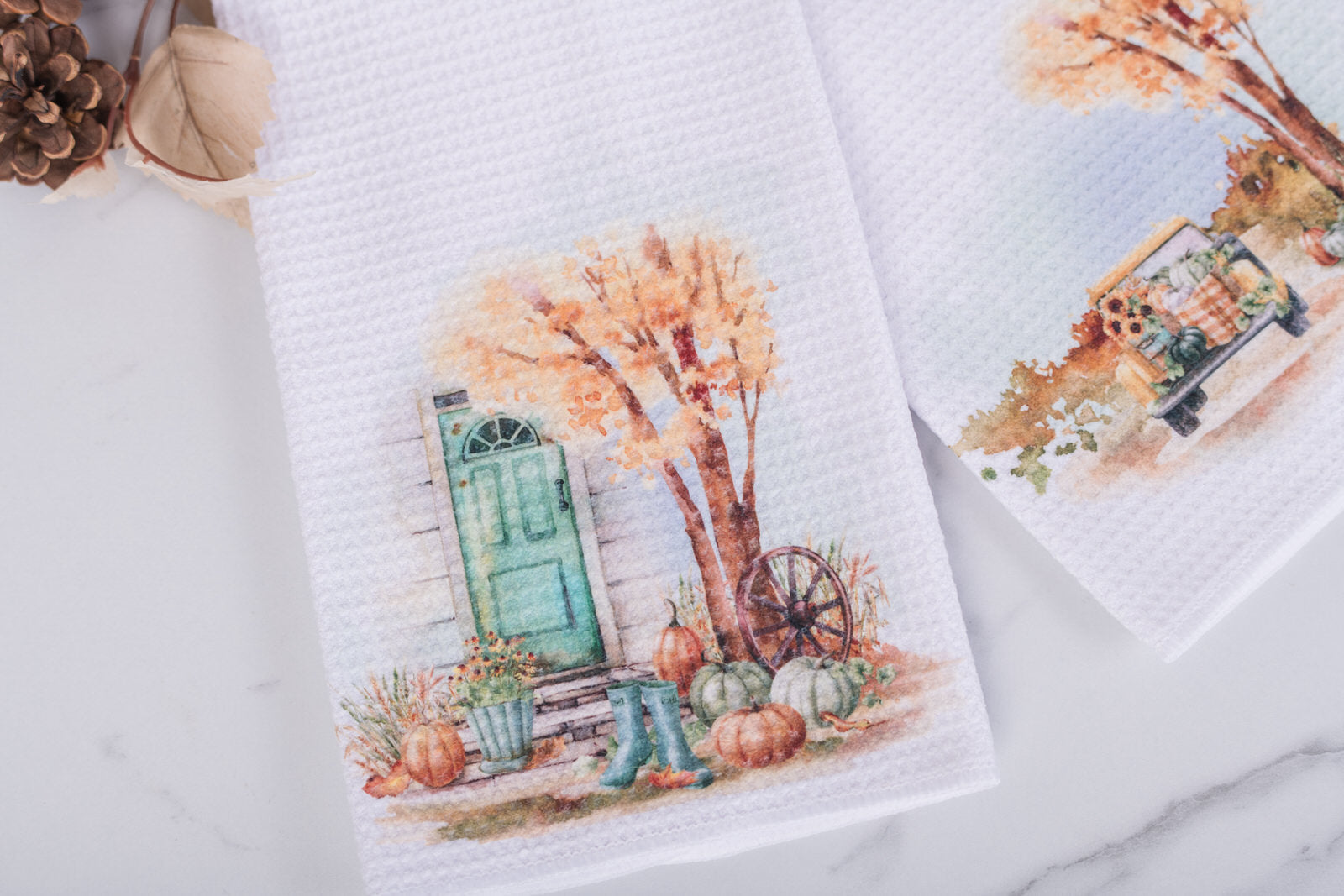 Decorative towels with autumn-themed designs featuring trees, pumpkins, and a door on a marble surface.