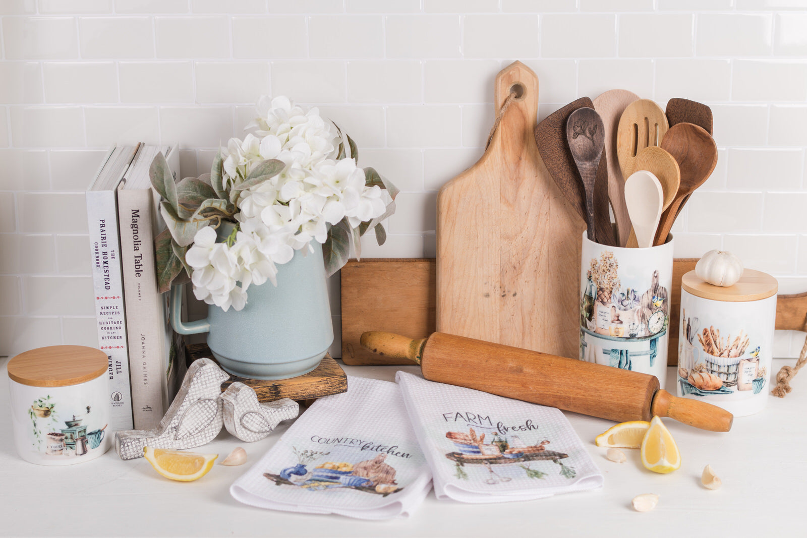 Country kitchen crock next to blue floral pitcher and rolling pin, and coordinating tea towels and canisters