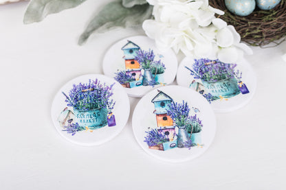 A set of four white ceramic coasters with a floral design and a French lavender theme, featuring a house and lavender bushes.