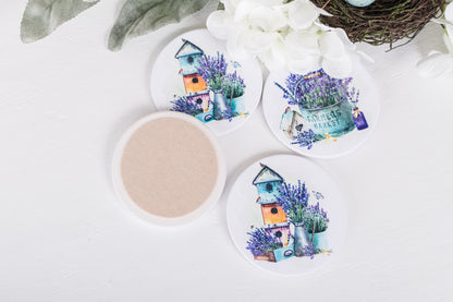 A set of four white ceramic coasters with a floral design and a French lavender theme, featuring a house and lavender bushes.
