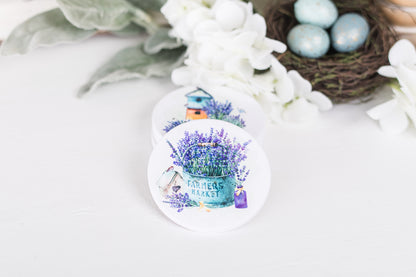 A set of four white ceramic coasters with a floral design and a French lavender theme, featuring a house and lavender bushes.