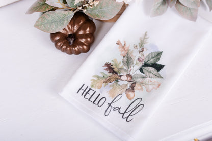 A white hand towel with a fall-themed print, including leaves and the text 'Hello Fall'.