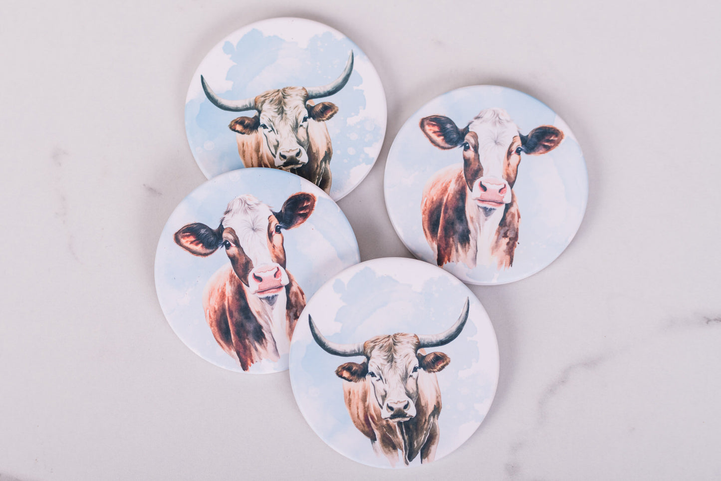 Four round coasters with cow illustrations on a light gray background