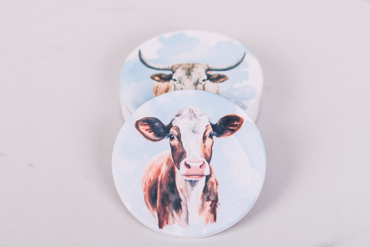 Two round coasters with cow designs on a light gray background