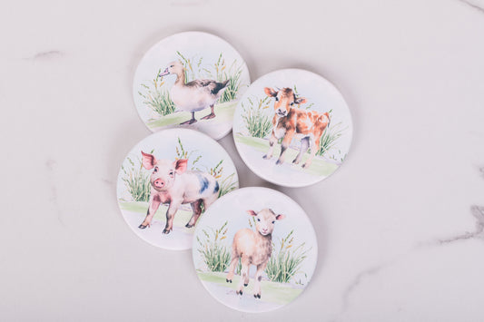 Set of four coasters with farm animal illustrations on a marble surface