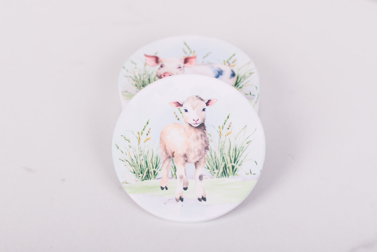 Two coasters with illustrations of lambs on a light gray background