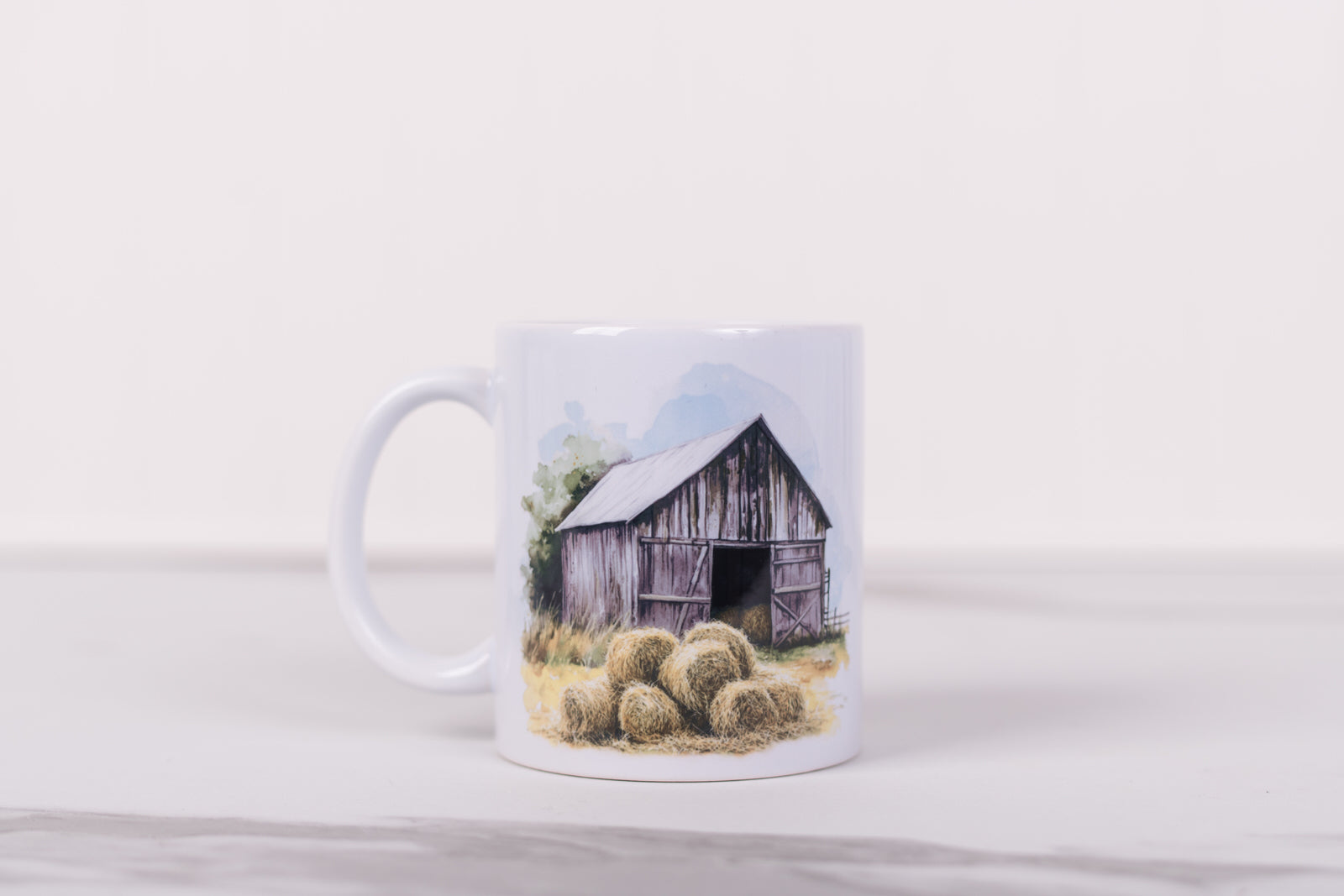 Mug with a design of a barn and hay bales on a white background