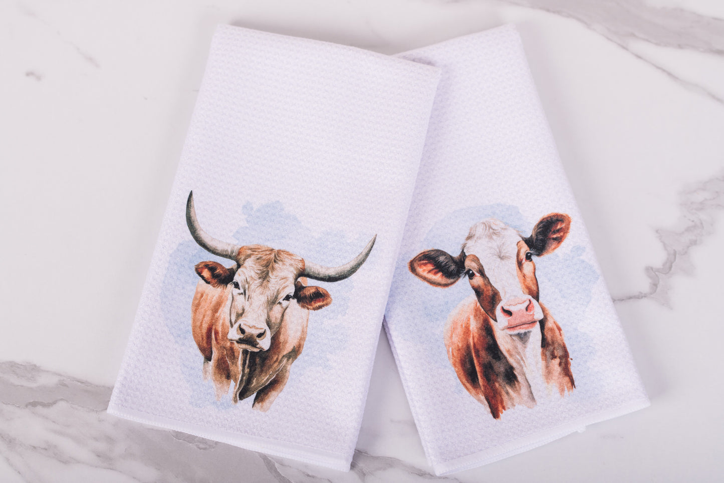Two towels with cow prints on a marble surface