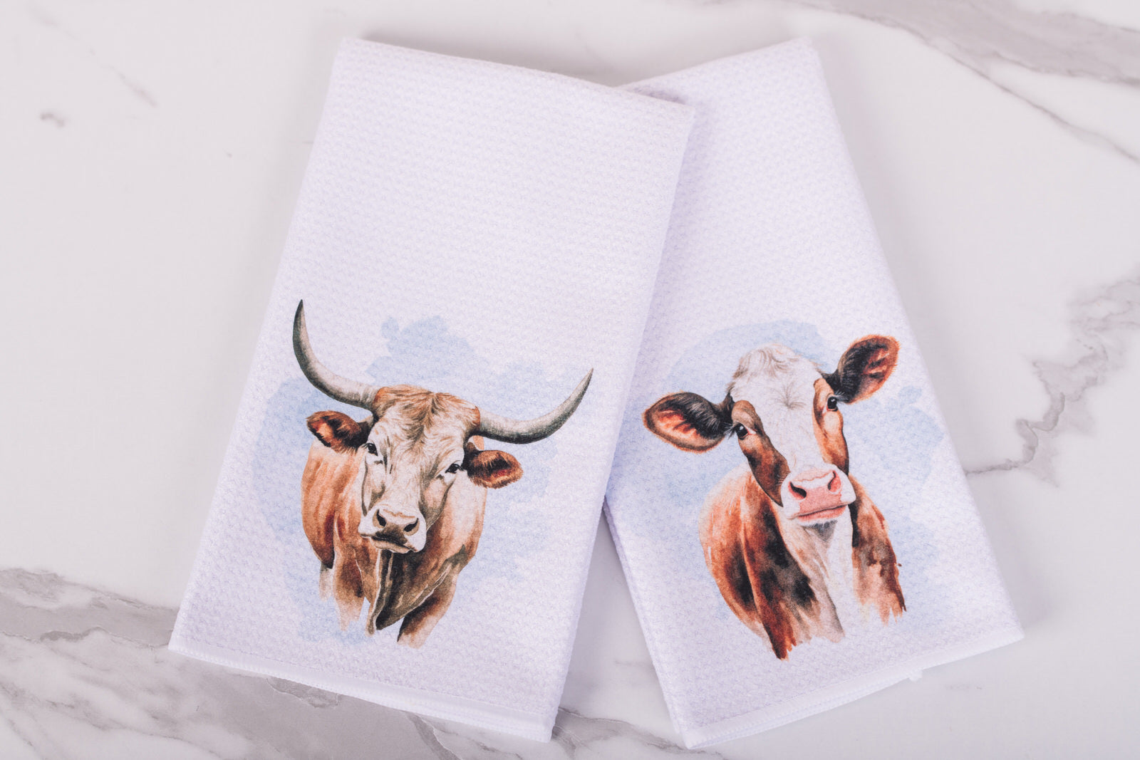 Two towels with cow prints on a marble surface