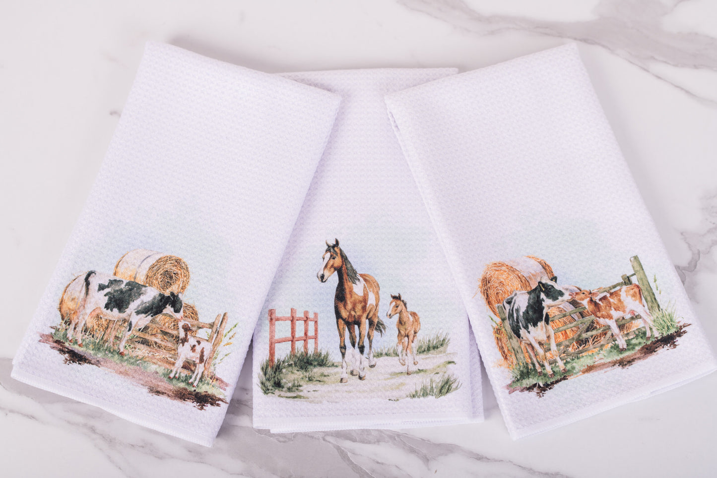 Three kitchen towels with farm animal designs on a white background