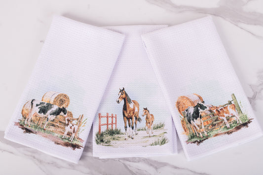 Three kitchen towels with farm animal designs on a white background