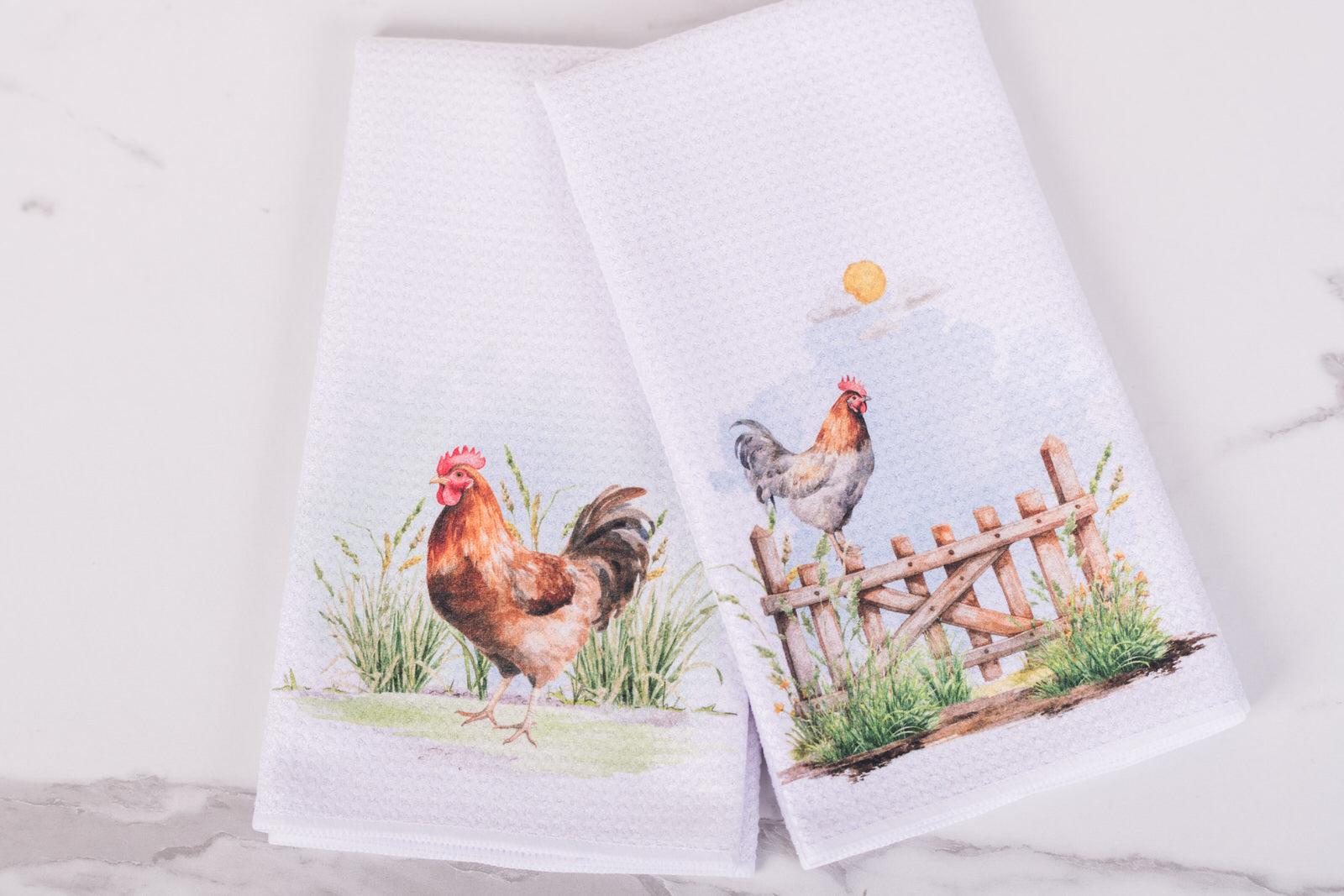 Two towels with farm-themed designs featuring chickens and a fence on a white background.