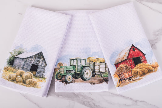 Three towels with farm-themed designs featuring a barn, tractor, and wagon on a white background.