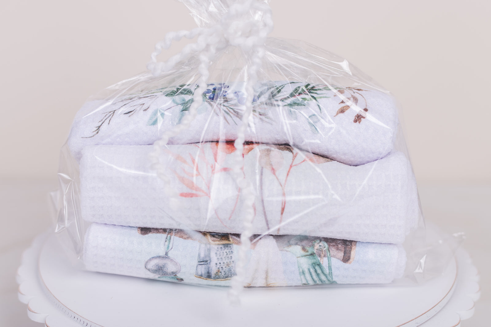 Stack of folded towels with floral patterns wrapped in clear plastic on a white surface