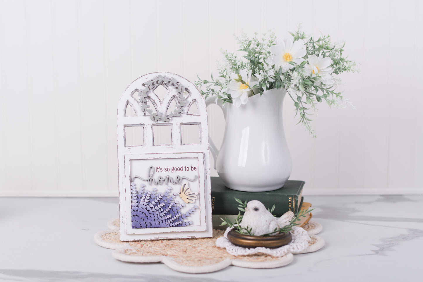 Decorative items including a white pitcher, lavender framed picture, and small bird figurine on a white surface.