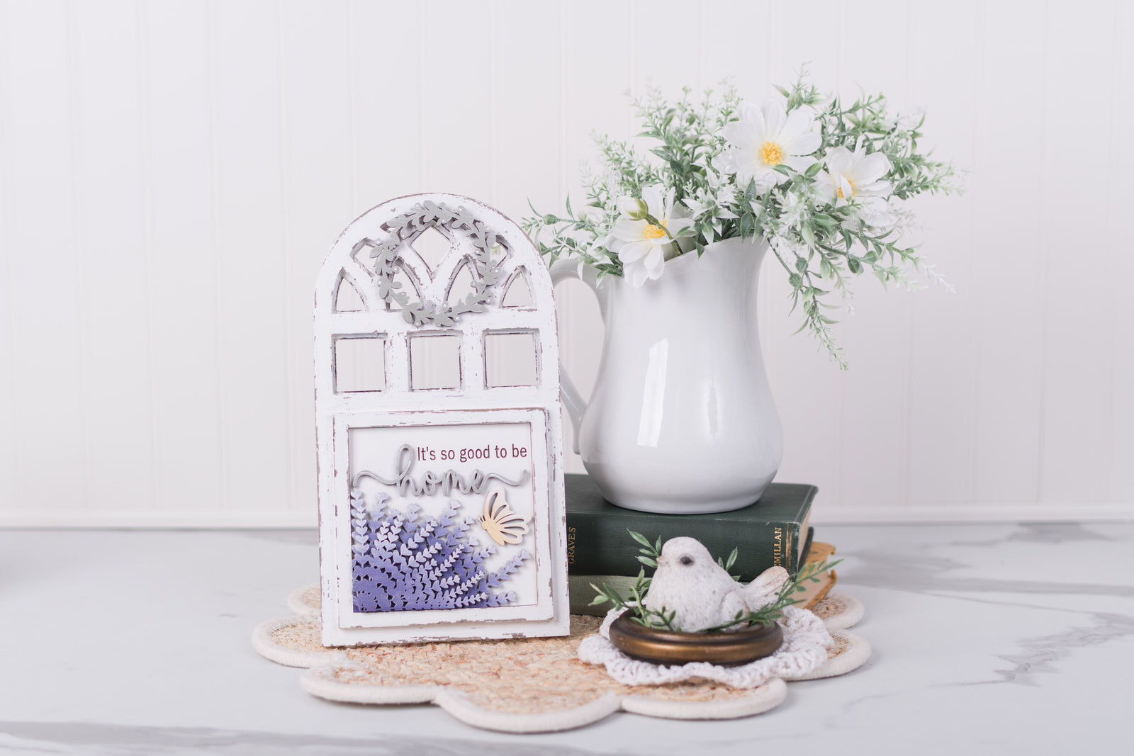 Decorative items including a white pitcher, lavender framed picture, and small bird figurine on a white surface.