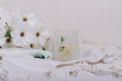 White flowers and a candle jar with lemons on a white surface with a blurred background