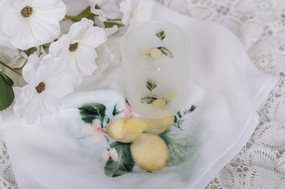  decorative, frosted candle jar, sitting on a lemon hand, towel with florals and a lace background 