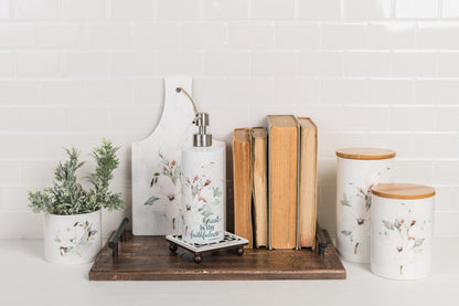 Decorative wood tray styled with books, a plant, and magnolia containers against a white tiled wall.