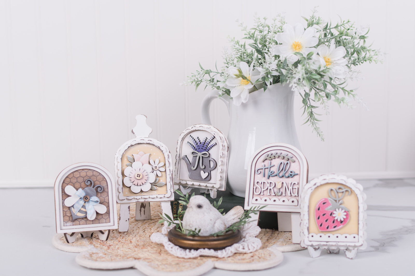Decorative spring-themed miniature arch signs with flowers and a bird on a white surface.