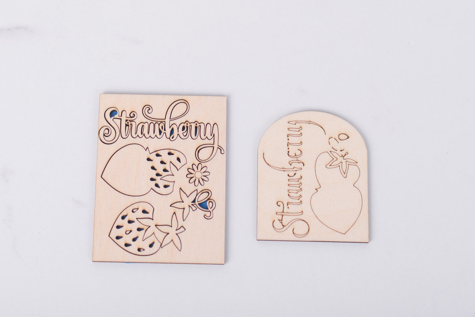 Two wooden strawberry-shaped signs with engraved designs on a light gray background