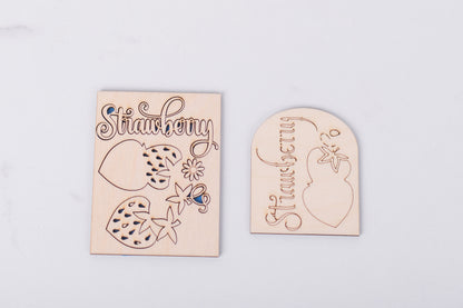 Two wooden strawberry-shaped signs with engraved designs on a light gray background