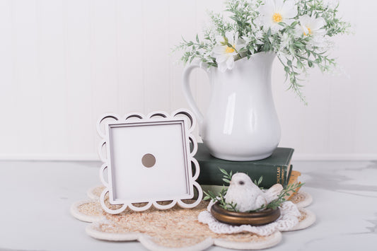 White pitcher with flowers, DIY picture frame, Kit and small bird figurine on a textured surface.