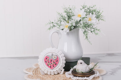 Decorative items include a white pitcher with flowers, a scallop frame with a strawberry insert and a small bird figurine on a textured surface.