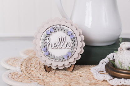 Decorative sign with 'hello' text on a stand, placed on a textured surface with a blurred background.