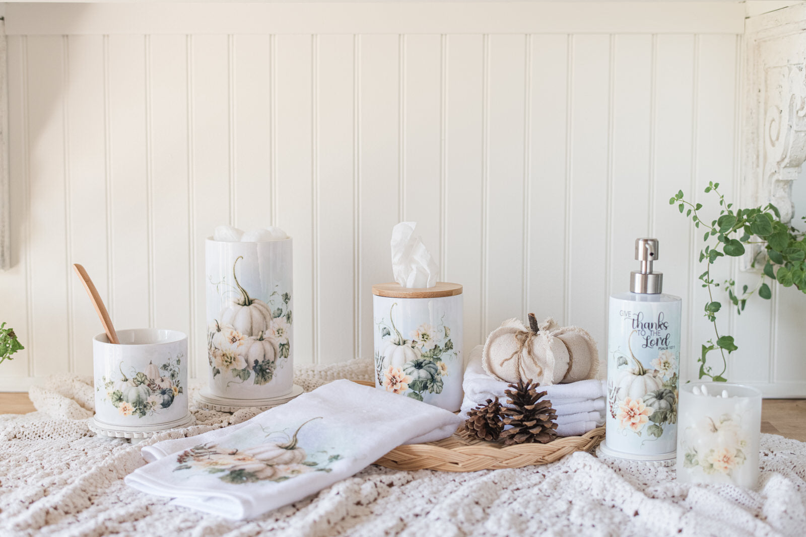 Decorative fall canisters styled for a bathroom with a ceramic tissue holder, hand towel, soap dispenser on a wicker tray with pinecones and a pumpkin